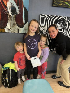 Dental staff posing with three young siblings after their checkup